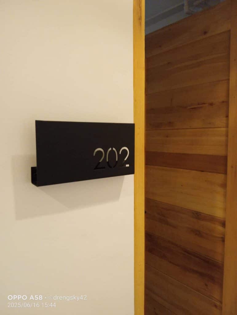 Acrylic room signage 202 black cut-out on white wall by wooden door in Quezon City, by M&G Global Ads.