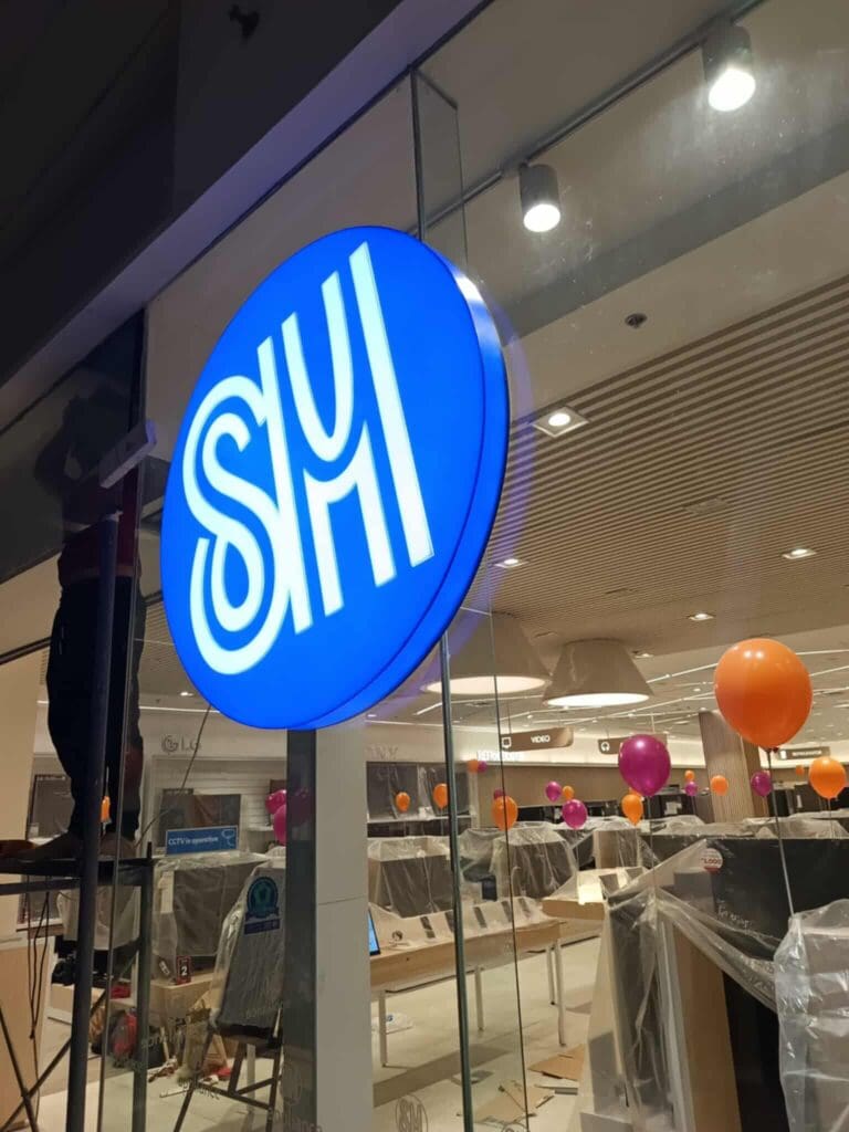 Acrylic indoor signage with white SM letters on blue, glass wall mounted at a new store in Philippines by sign maker Philippines, M&G Global Ads.