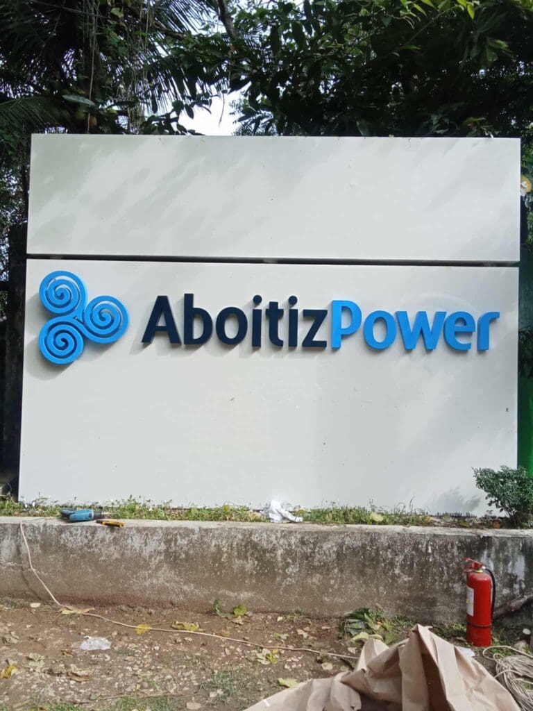 AboitizPower outdoor signage in Makati with blue logo, greenery, and fire extinguisher by M&G Global Ads.