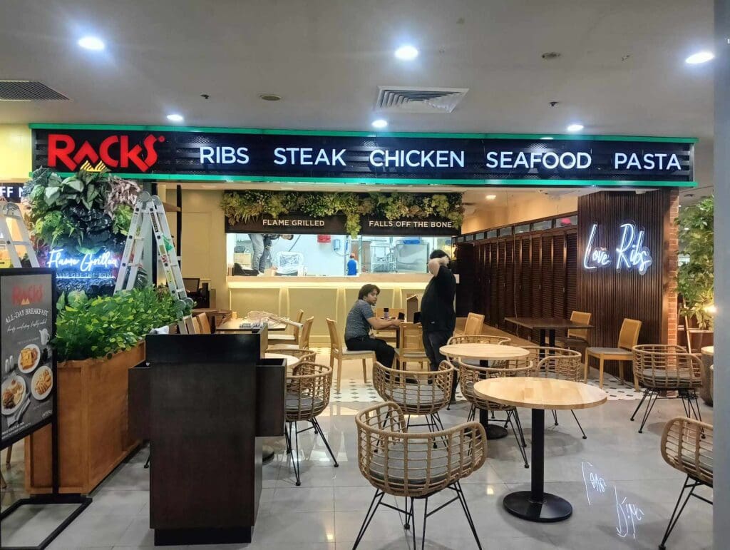 Neon Love Ribs signage and menu board at restaurant interior in BGC with M&G Global Ads branding, plants, tables, diners.
