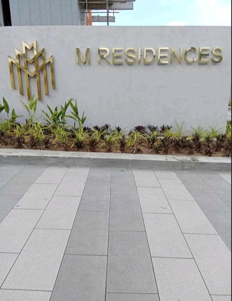 Exterior building signage for M Residences in Mandaluyong with brass logo and plants by M&G Global Ads.