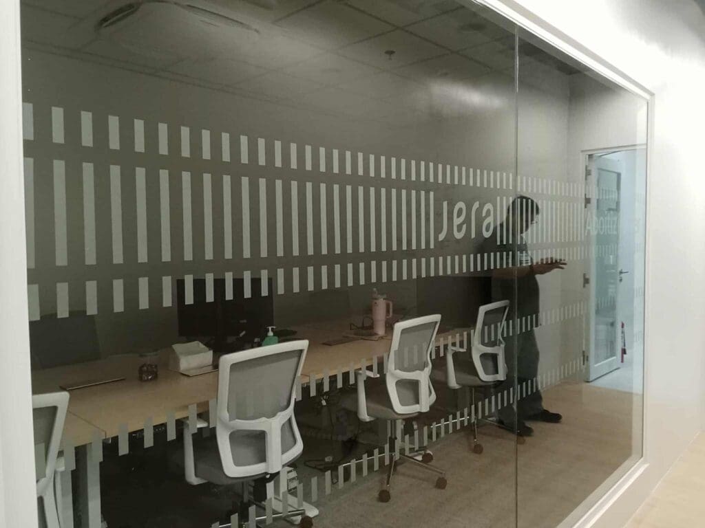 frosted sticker signage with partial text, white chairs, wooden desks in Makati meeting room. By M&G Global Ads.