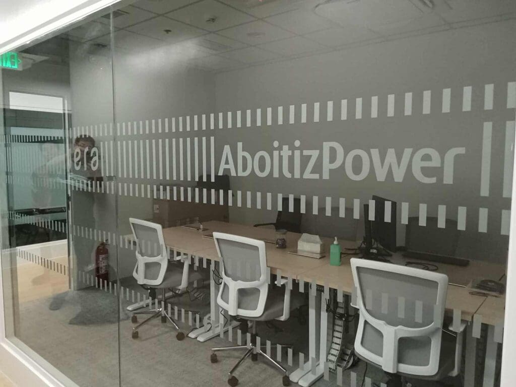 Office frosted sticker signage for AboitizPower in Makati, with desks, white chairs, and fire extinguisher by M&G Global Ads.