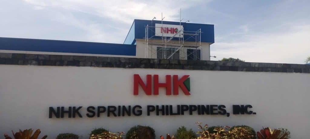 NHK Spring Philippines, Inc. outdoor signage on white building with blue roof in BGC, scaffold and plants by M&G Global Ads.
