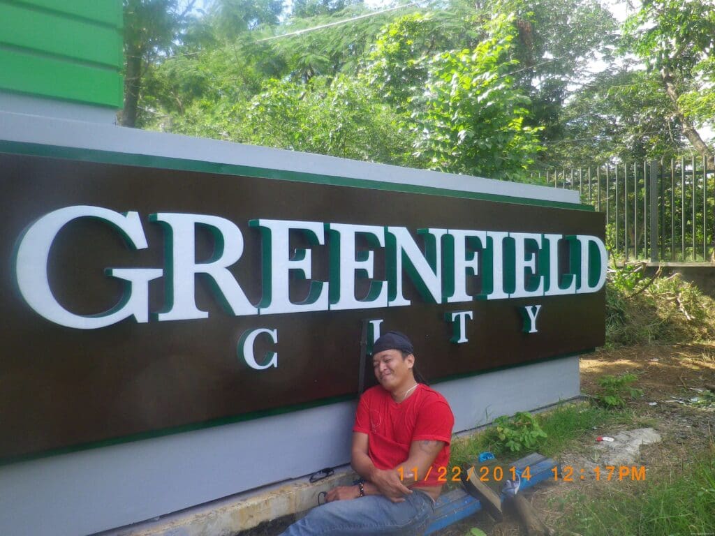 A man smiles by a Greenfield City outdoor building signage in Metro Manila. Sign maker Philippines by M&G Global Ads.