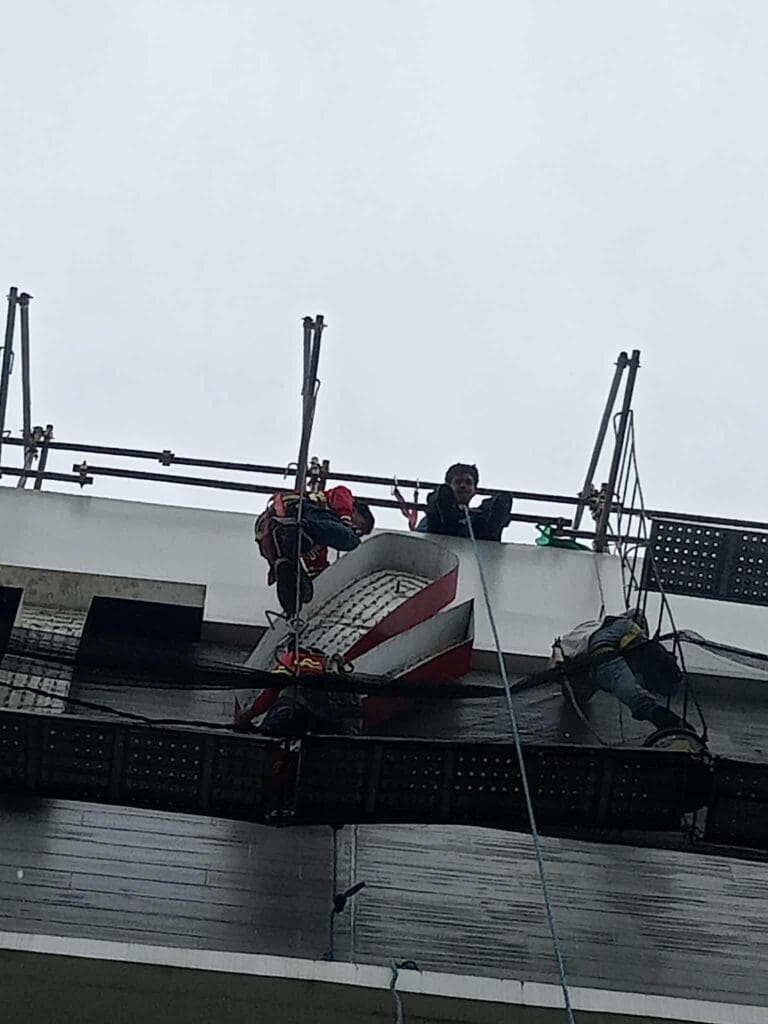 Three sign maker Philippines workers clean building outdoor signage, wearing safety harnesses in Metro Manila by M&G Global Ads.