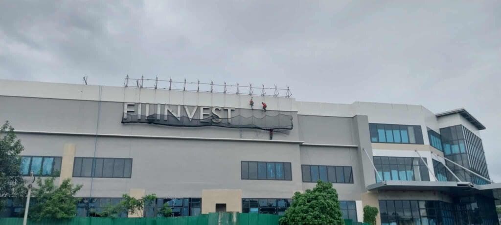 Workers installing acrylic building signage for FINVEST in Metro Manila. Sign maker Philippines by M&G Global Ads.