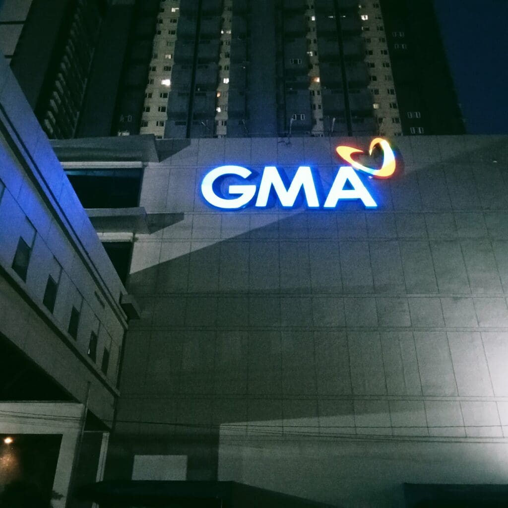 Illuminated LED building signage of GMA logo on high-rise exterior at night in Metro Manila by sign maker Philippines, by M&G Global Ads.