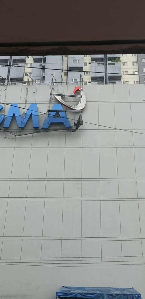 Worker suspended by ropes installs outdoor building signage on beige panels, Metro Manila, sign maker Philippines by M&G Global Ads.