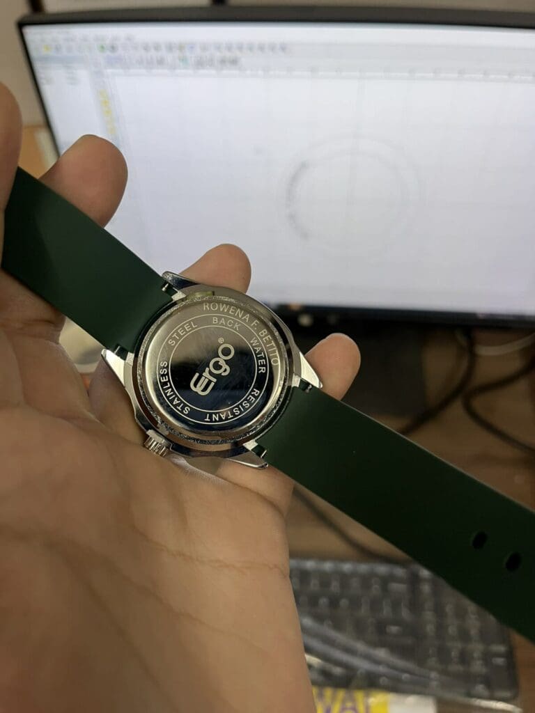 A hand holds a wristwatch with engraved back, showcasing engraving signage by sign maker Philippines. Metro Manila by M&G Global Ads.