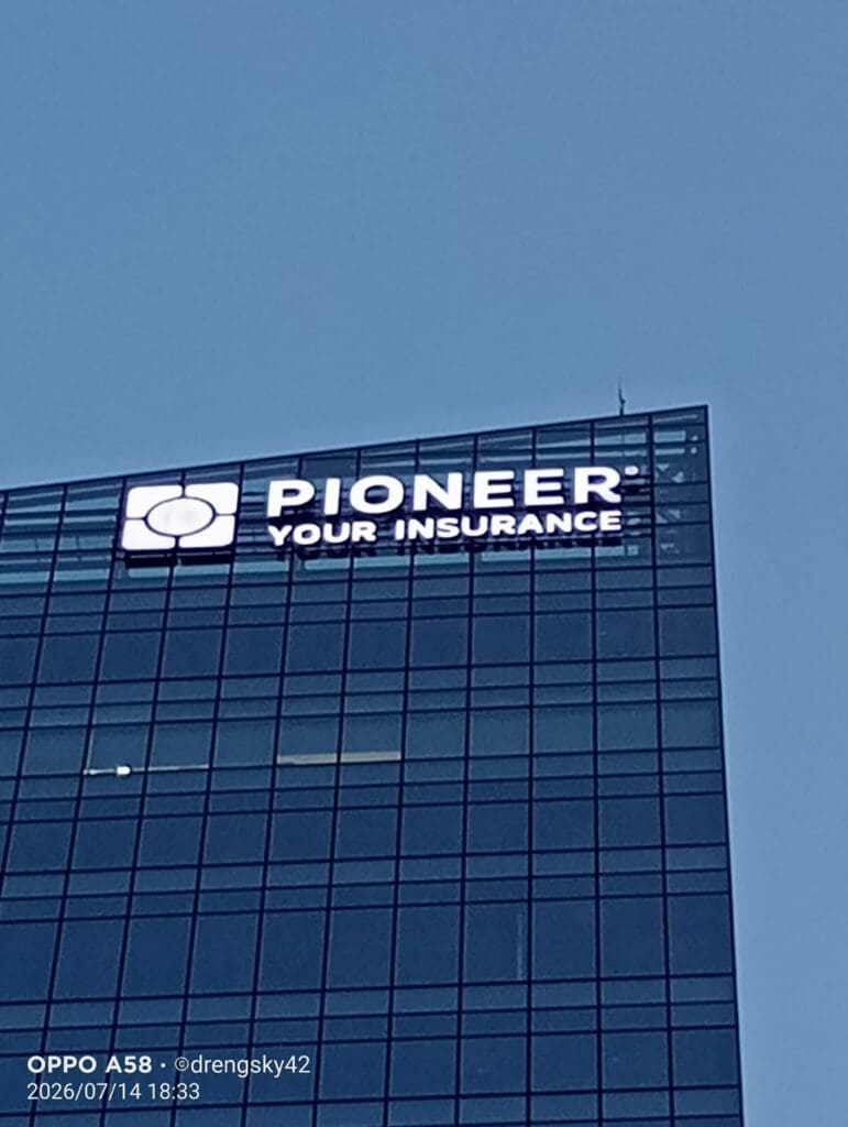 A tall glass building at dusk in Metro Manila features an outdoor LED building signage that reads "Pioneer Your Insurance" near the top, with a cloudy sky in the background. Sign maker Philippines by M&G Global Ads.