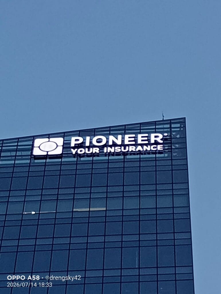 A tall glass office building with an illuminated outdoor LED signage for PIONEER YOUR INSURANCE against a clear blue evening sky, located in the Philippines, sign maker Philippines by M&G Global Ads.