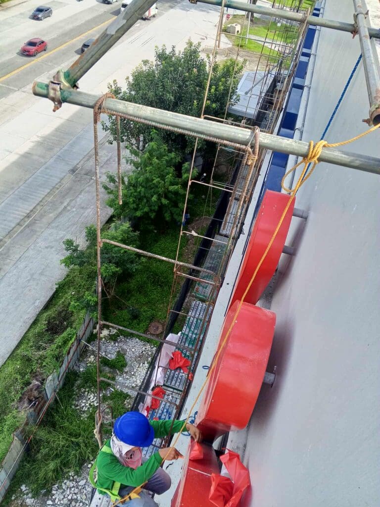 A worker climbs scaffolding to install building signage, stainless steel material, Metro Manila sign maker Philippines by M&G Global Ads.