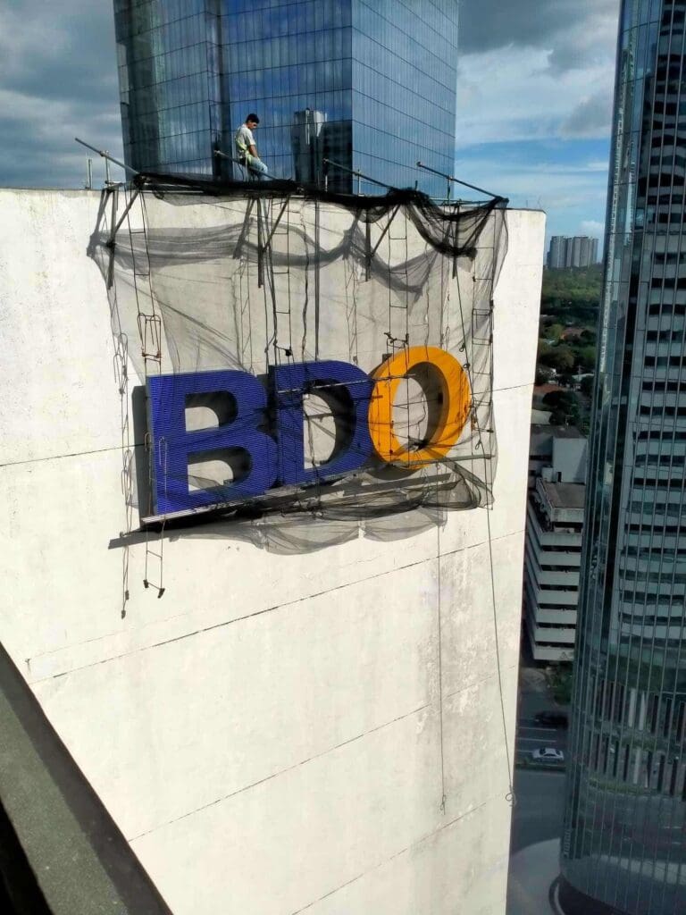 A worker installs BDO outdoor building acrylic signage with blue and yellow letters in Metro Manila, sign maker Philippines by M&G Global Ads.