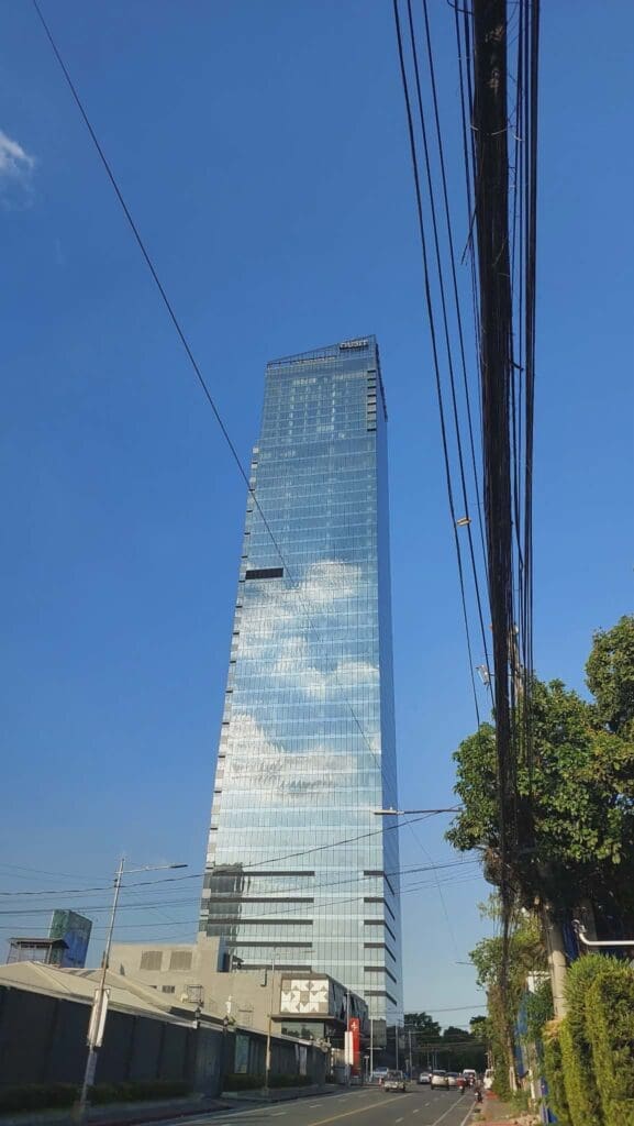 Acrylic building signage on tall glass skyscraper, city street view, Metro Manila, sign maker Philippines by M&G Global Ads.