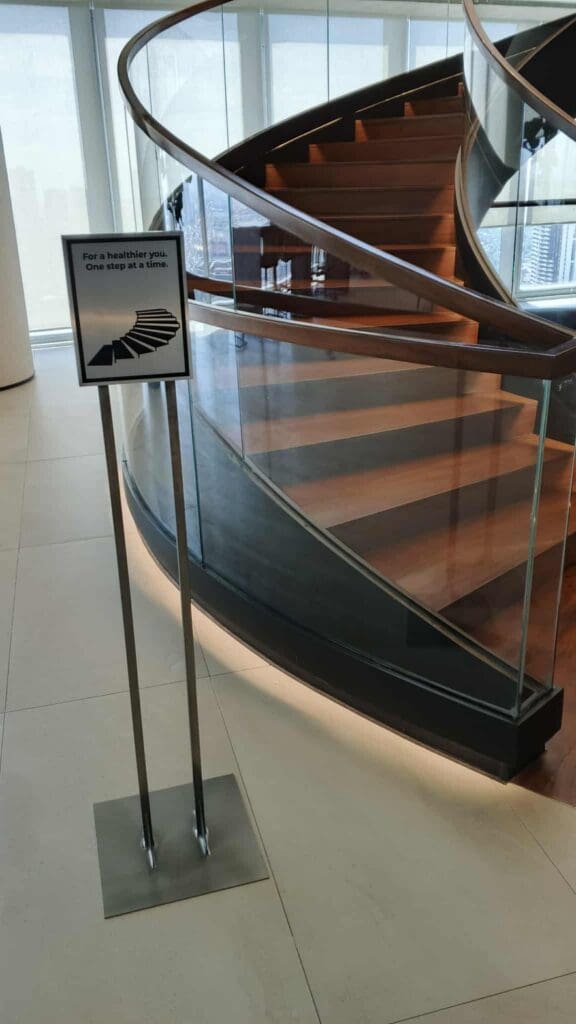 Acrylic indoor wayfinding sign with health message by spiral wooden staircase, Metro Manila. Sign maker Philippines by M&G Global Ads.