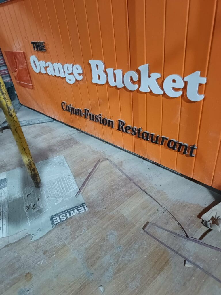 Acrylic wall signage for The Orange Bucket Cajun-Fusion Restaurant with white 3D letters, Metro Manila. Sign maker Philippines by M&G Global Ads.