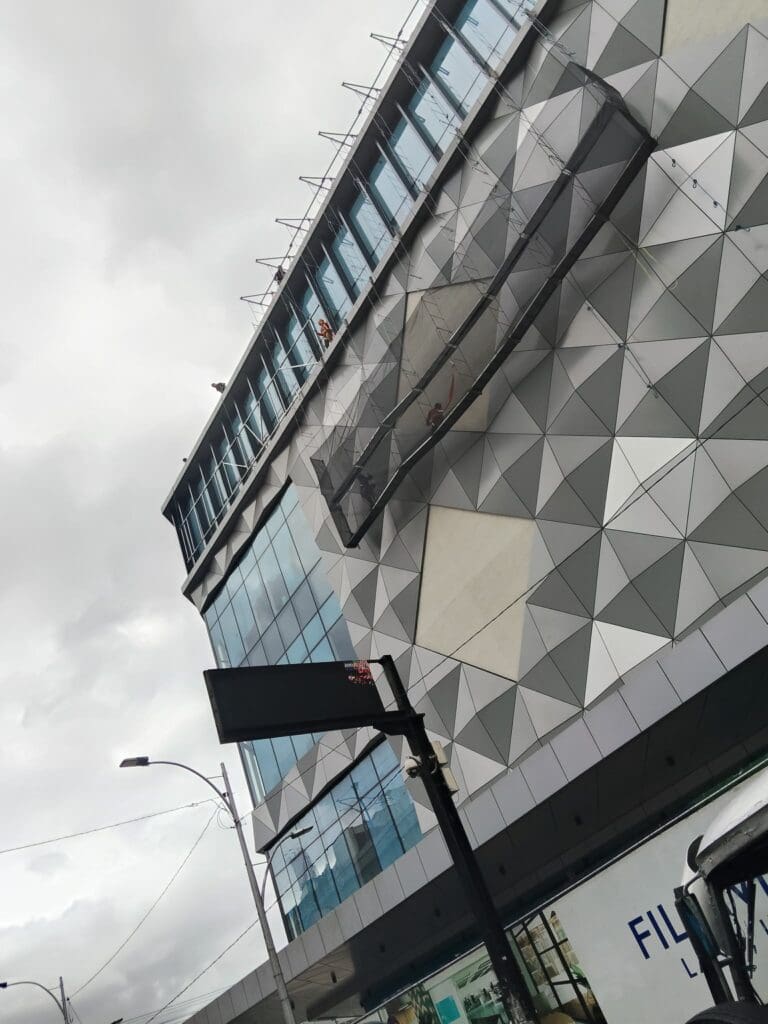 Building signage installation on a geometric facade, worker on platform, Metro Manila sign maker Philippines by M&G Global Ads.