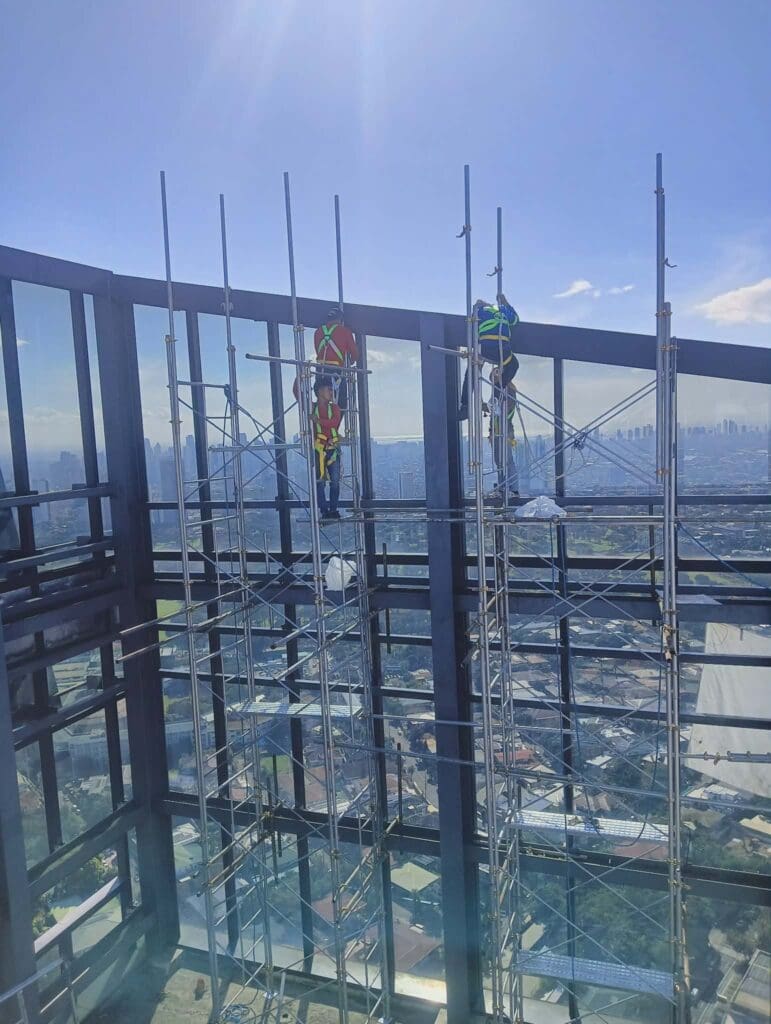 Building signage installation on tall glass exterior by three construction workers, Metro Manila, sign maker Philippines by M&G Global Ads.