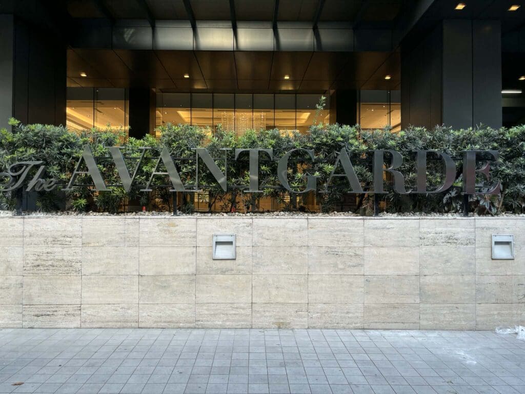 Building signage with large black acrylic letters "The AVANTGARDE" on beige stone wall, Metro Manila, sign maker Philippines by M&G Global Ads.