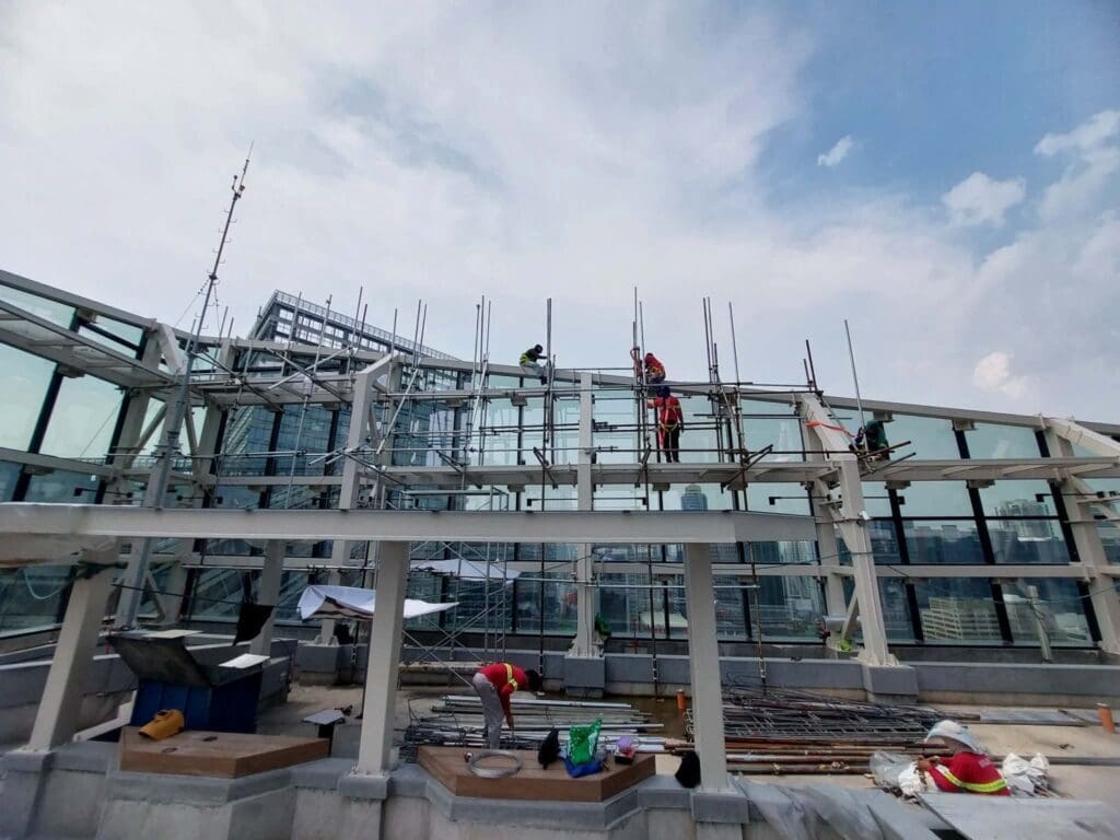 Construction workers install building signage with glass panels and steel beams on rooftop, high-rises in Metro Manila—sign maker Philippines by M&G Global Ads.