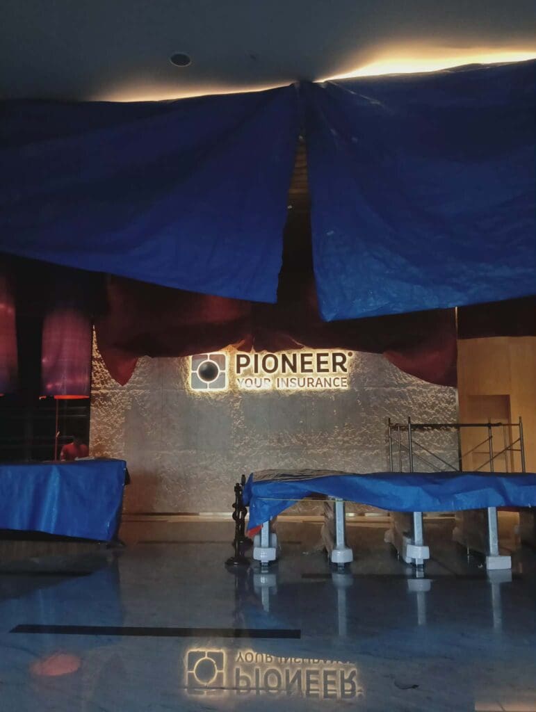 Dimly lit lobby with LED indoor building sign “PIONEER YOUR INSURANCE.” Scaffolding visible. Sign maker Philippines by M&G Global Ads.
