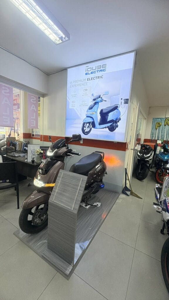 Electric scooter in showroom with acrylic promotional signage, office desks, and motorbikes. Sign maker Philippines by M&G Global Ads.