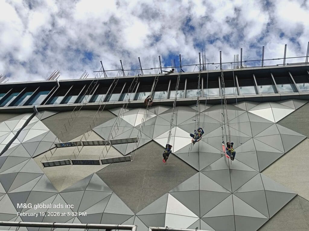 Four workers on ropes install building signage, geometric facade, outdoor aluminum sign maker Philippines by M&G Global Ads.
