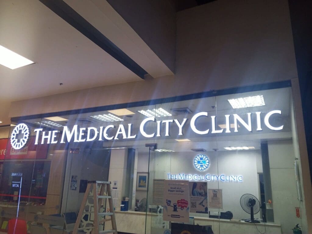 Front view of The Medical City Clinic in Metro Manila with acrylic illuminated building signage, glass walls, a ladder outside, and reception area visible inside; sign maker Philippines by M&G Global Ads.