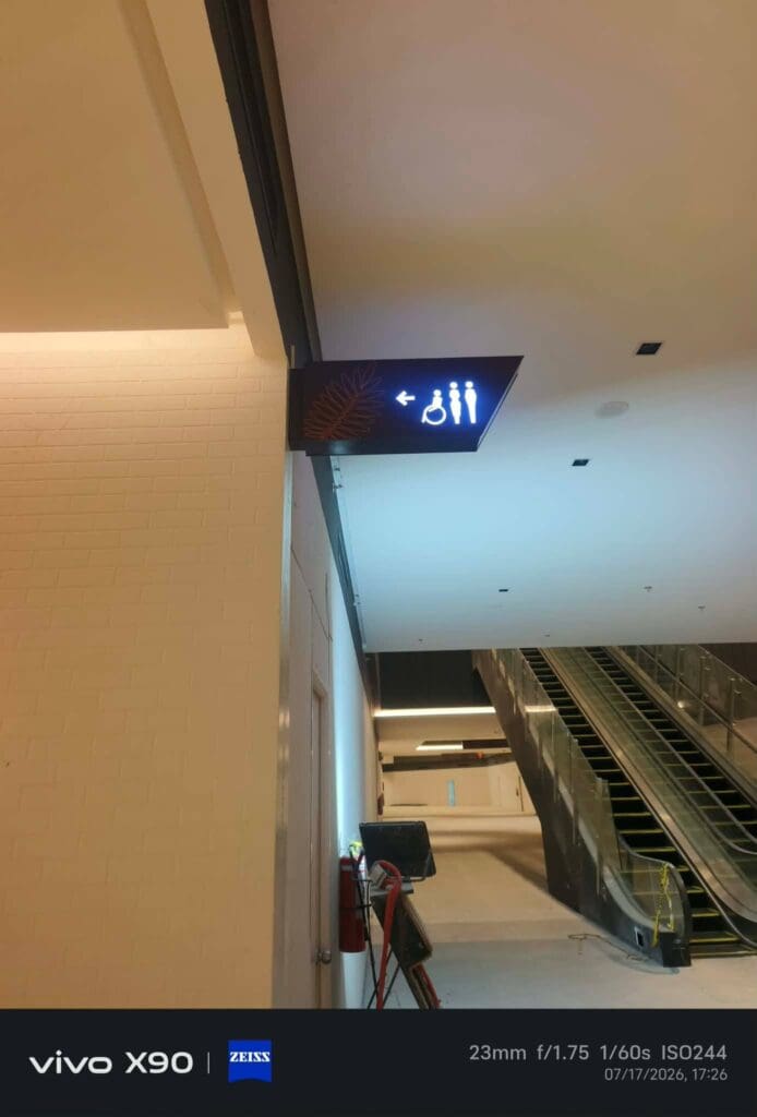 Indoor acrylic restroom wayfinding signage with male, female, and accessible symbols points left in a mall near an escalator in the Philippines, sign maker Philippines by M&G Global Ads.