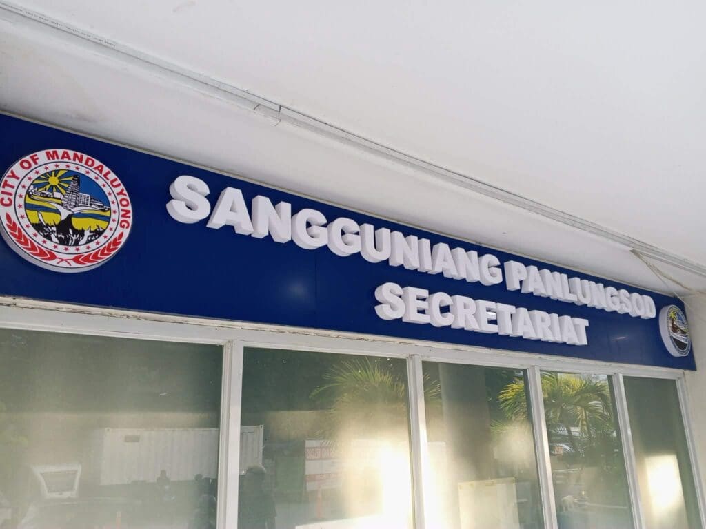 Indoor acrylic room signage for Sangguniang Panlungsod Secretariat above glass doors, featuring the City of Mandaluyong seal and another emblem, located in Mandaluyong, Metro Manila. Sign maker Philippines by M&G Global Ads.