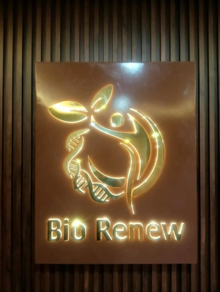 LED acrylic "Bio Renew" signage on a wood panel background in Metro Manila, featuring a glowing logo with a stylized leaf, DNA helix, and human figure symbolizing health, nature, and biotechnology; sign maker Philippines by M&G Global Ads.
