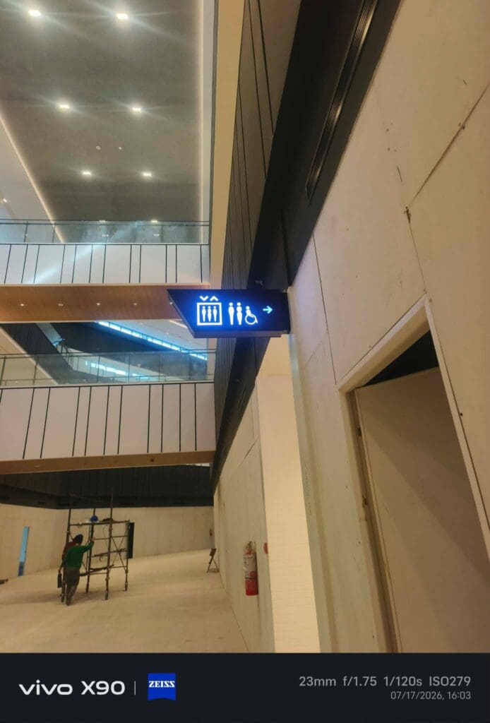LED acrylic restroom signage displaying men, women, accessible restroom, and baby changer icons in a modern indoor building environment with a person working on scaffolding in the background, Metro Manila, sign maker Philippines by M&G Global Ads.