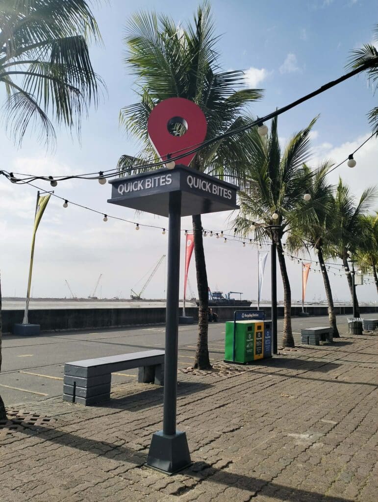 Outdoor acrylic “Quick Bites” food signage at waterfront walkway, palm trees, benches; sign maker Philippines by M&G Global Ads.