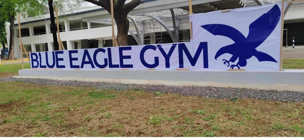 Outdoor building banner signage for BLUE EAGLE GYM with blue eagle graphic, grass, trees, Metro Manila. Sign maker Philippines by M&G Global Ads.