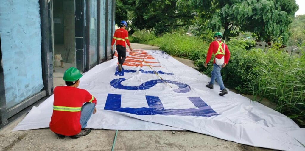 Outdoor building banner signage installation by construction workers in Metro Manila, sign maker Philippines by M&G Global Ads.