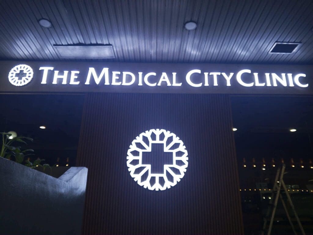 Outdoor LED acrylic signage for The Medical City Clinic featuring a brightly lit sign with a glowing circular logo and cross above the entrance at night, Metro Manila, sign maker Philippines by M&G Global Ads.