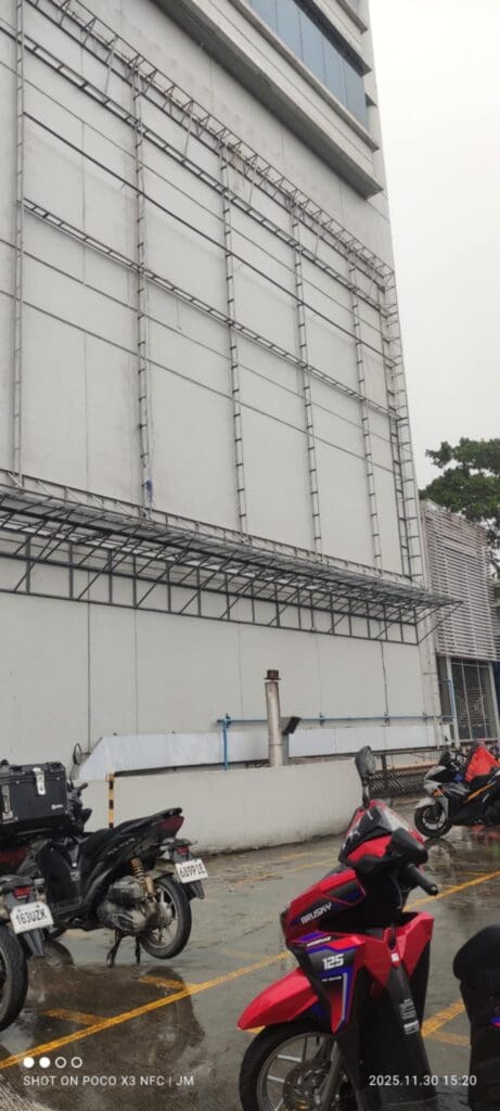 Outdoor parking lot in Metro Manila with empty metal frames for building signage, motorcycles parked; sign maker Philippines by M&G Global Ads.