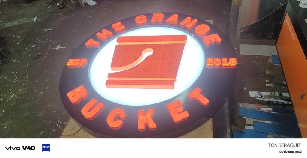 Round acrylic LED signage for The Orange Bucket, glowing orange and white, workshop view, Metro Manila. Sign maker Philippines by M&G Global Ads.