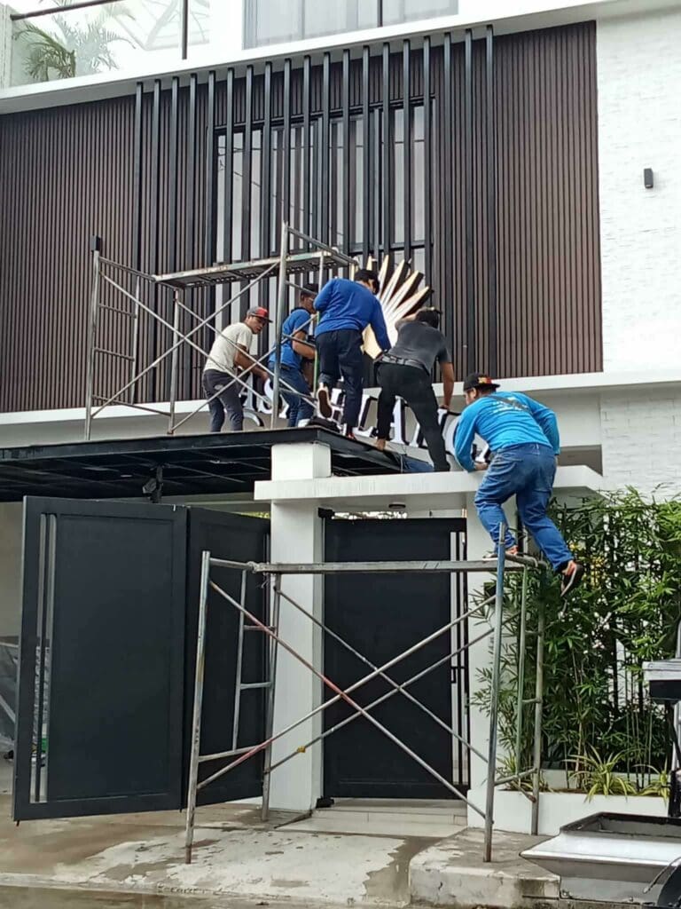 Six workers install a large stainless steel building signage on a modern exterior in Metro Manila, sign maker Philippines by M&G Global Ads.