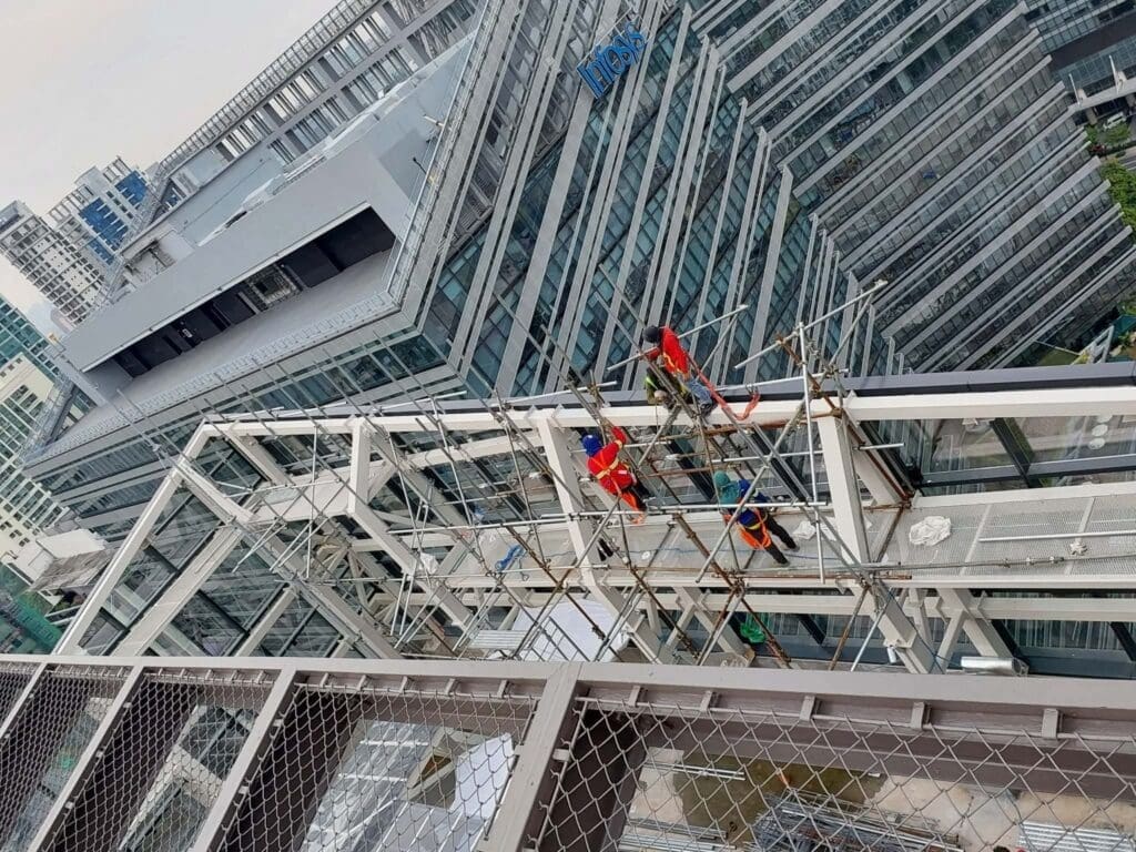 Three workers install outdoor building signage on glass office in Metro Manila cityscape, sign maker Philippines by M&G Global Ads.