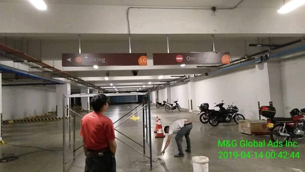 Two men work near acrylic parking wayfinding signs in an indoor garage, Metro Manila. Sign maker Philippines by M&G Global Ads.