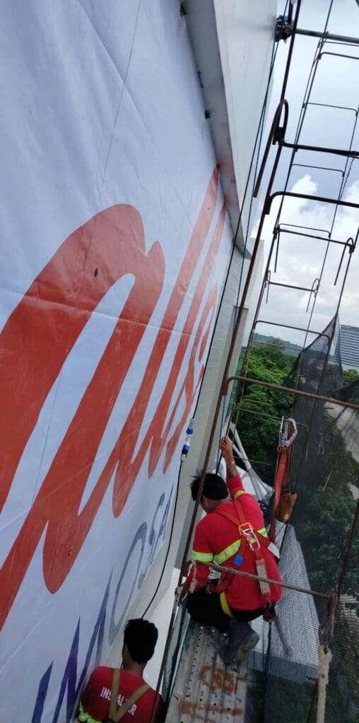 Two workers install outdoor billboard signage on a building in Metro Manila—sign maker Philippines by M&G Global Ads.