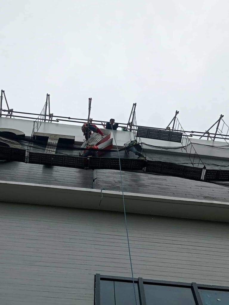 Two workers install outdoor building signage on scaffolding, overcast sky, Metro Manila, sign maker Philippines by M&G Global Ads.