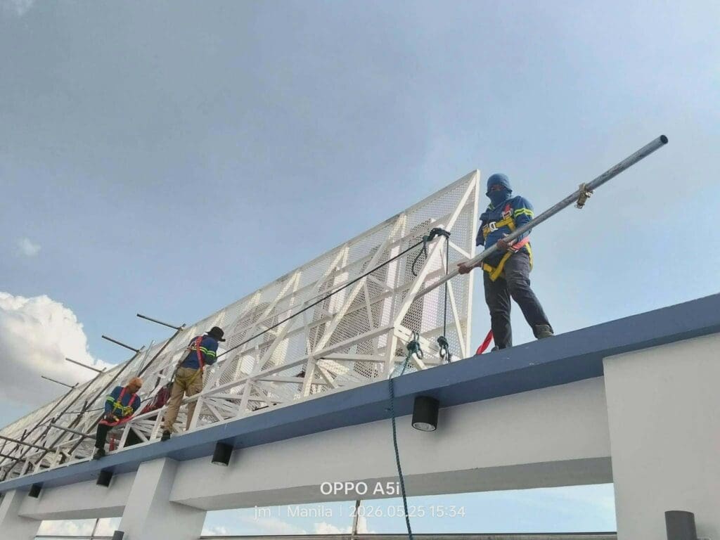 Two workers installing a large outdoor aluminum billboard sign in safety gear atop a building, Metro Manila, by sign maker Philippines M&G Global Ads.