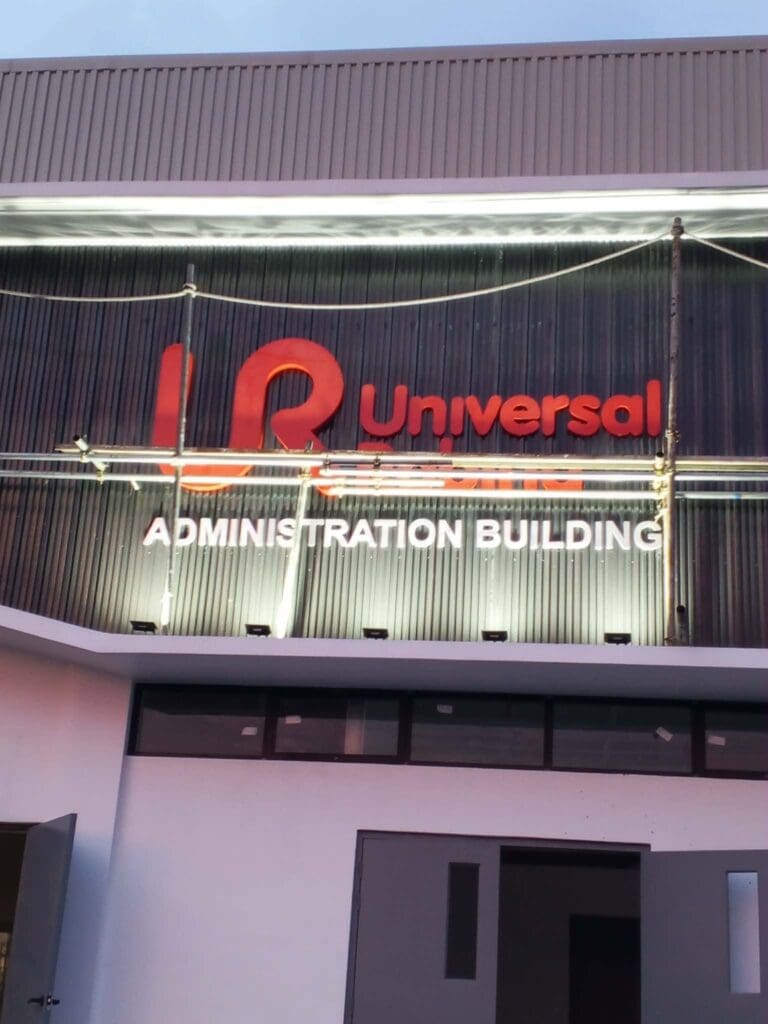 Universal ADMINISTRATION BUILDING outdoor building sign with red and white acrylic letters mounted above the entrance, displayed on a corrugated metal façade with glass windows, Metro Manila, sign maker Philippines by M&G Global Ads.
