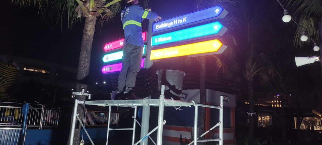 Worker adjusts colorful outdoor LED wayfinding signage at night, Metro Manila. Sign maker Philippines by M&G Global Ads.