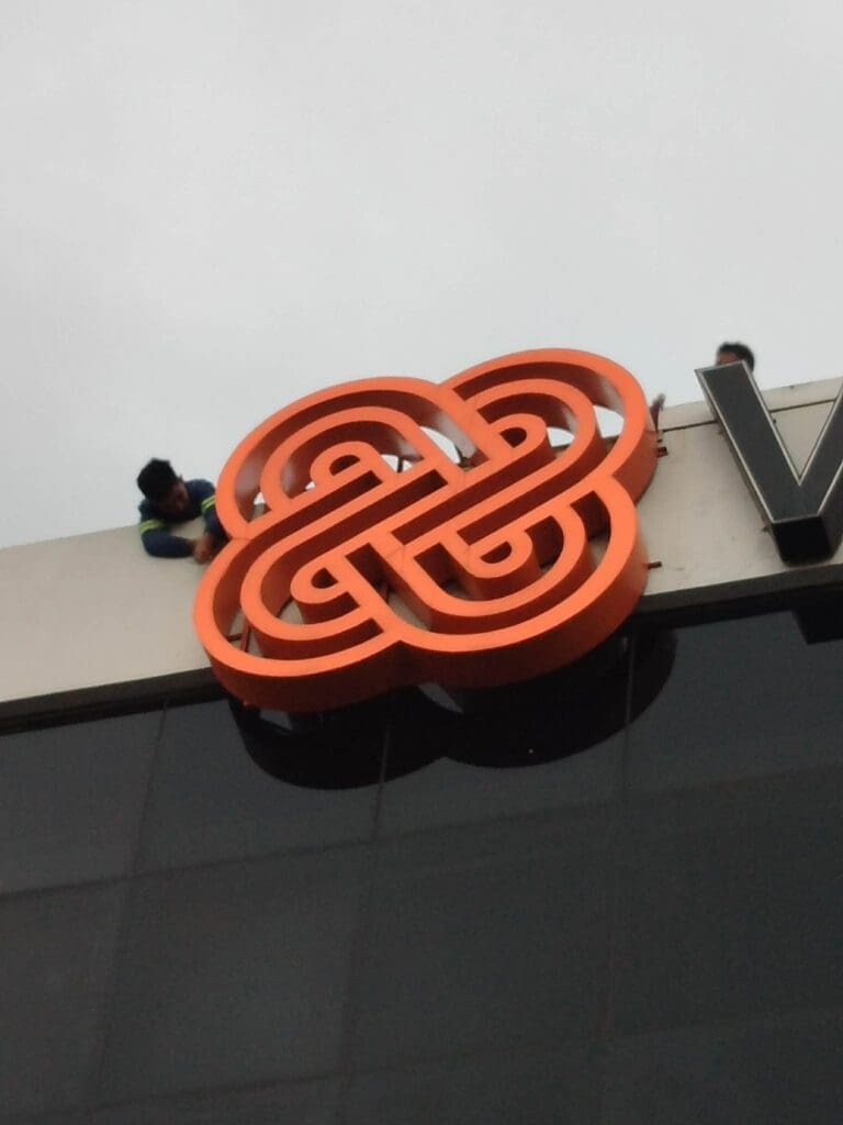 Worker in safety harness installs large outdoor acrylic logo signage on building facade, Metro Manila sign maker Philippines by M&G Global Ads.