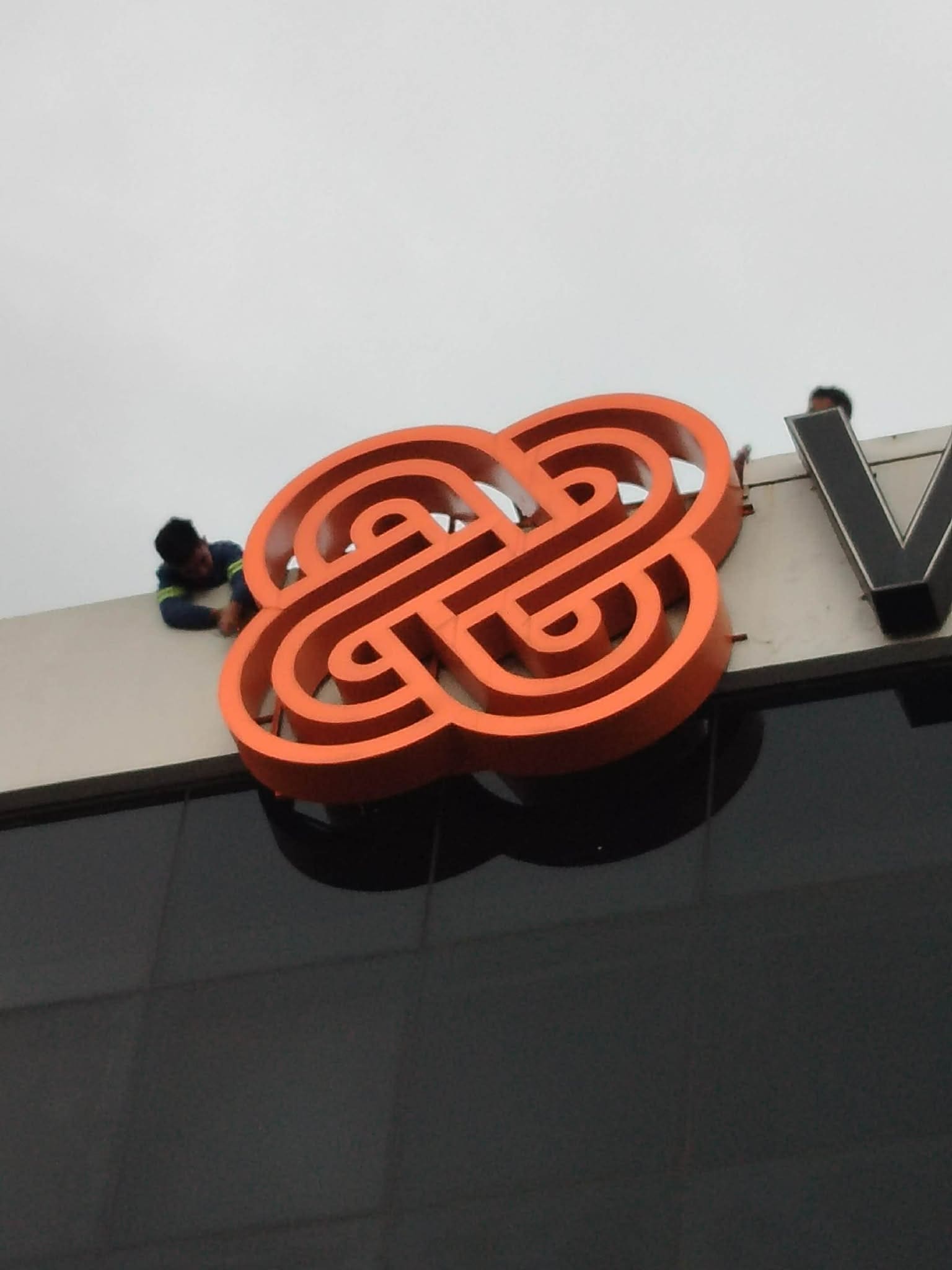 Worker in safety harness installs large outdoor acrylic logo signage on building facade, Metro Manila sign maker Philippines by M&G Global Ads.
