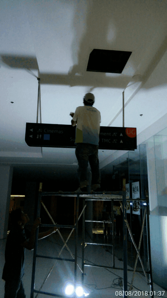 Worker on scaffolding installs indoor ceiling signage, likely acrylic, Metro Manila, sign maker Philippines by M&G Global Ads.